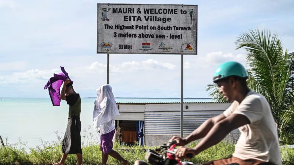 Locals walk past a sign showing the highest point above sea level in Tarawa, the country's main island. Photo - CNA/Jack Board