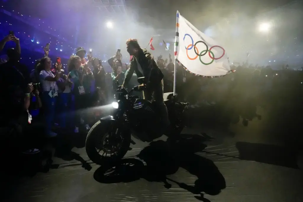 Tom Cruise rides a motorbike with the Olympic flag attached past athletes during the 2024 Summer Olympics closing ceremony at the Stade de France, Sunday, Aug. 11, 2024, in Saint-Denis, France. (AP Photo/Ashley Landis)